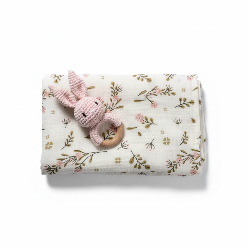 Floral muslin baby wrap with pink crochet rattle on white background