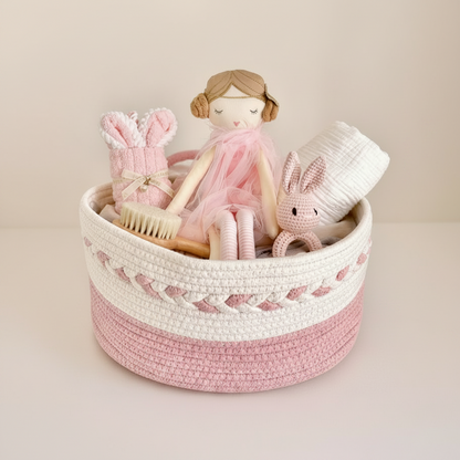 Pink and white woven baby gift hamper with a cloth doll in a pink dress, white blanket muslin, crocheted bunny rattle, wooden brush and mini bunny towel