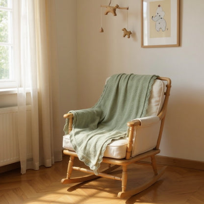Sage soft knit baby blanket with subtle openwork patter styled on a wooden rocking chair