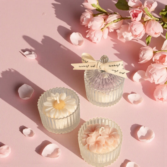 Decorative candles with floral designs on a pink background with flowers and petals.