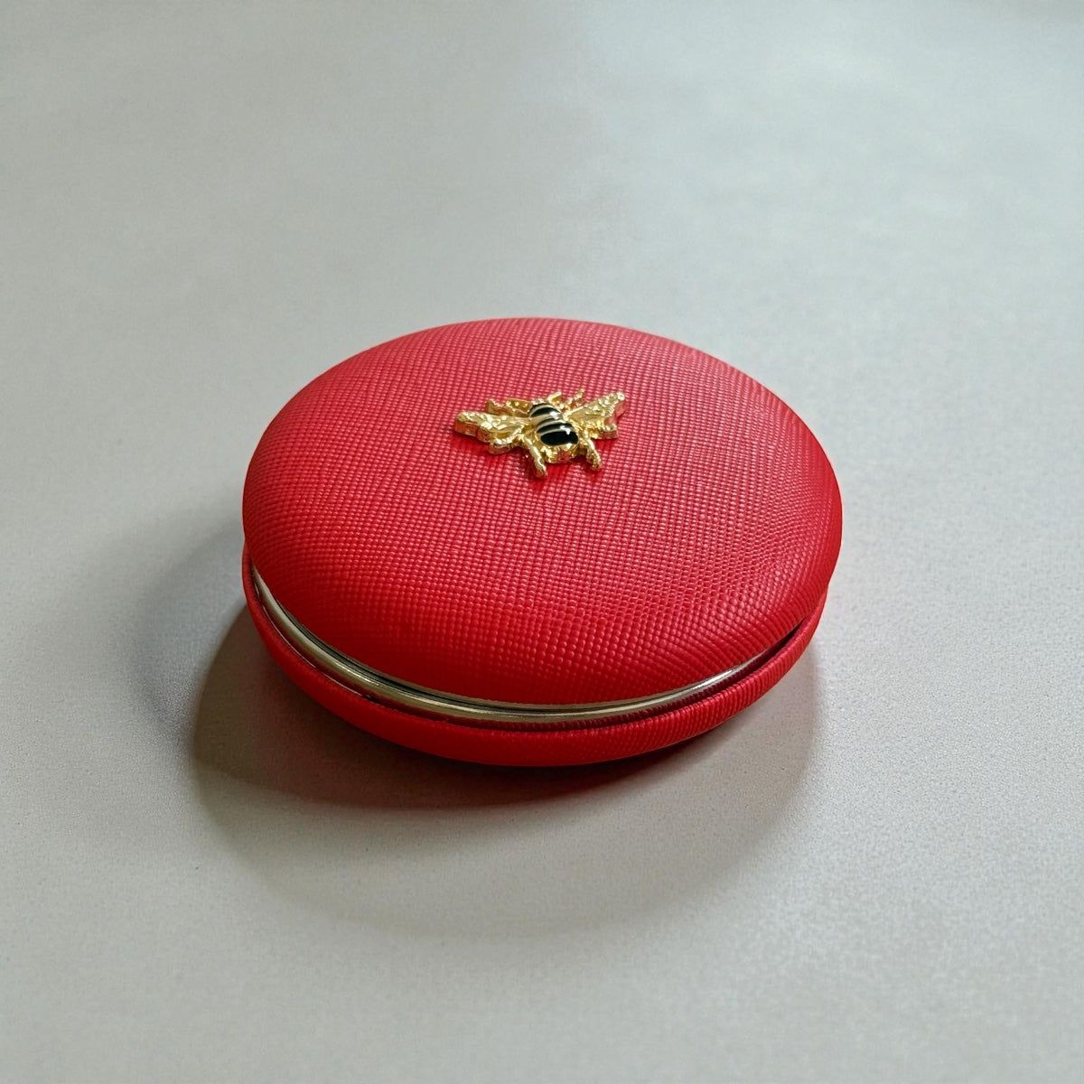 Red round dual- sided compact mirror with gold bee emblem, 1x and 2x magnification