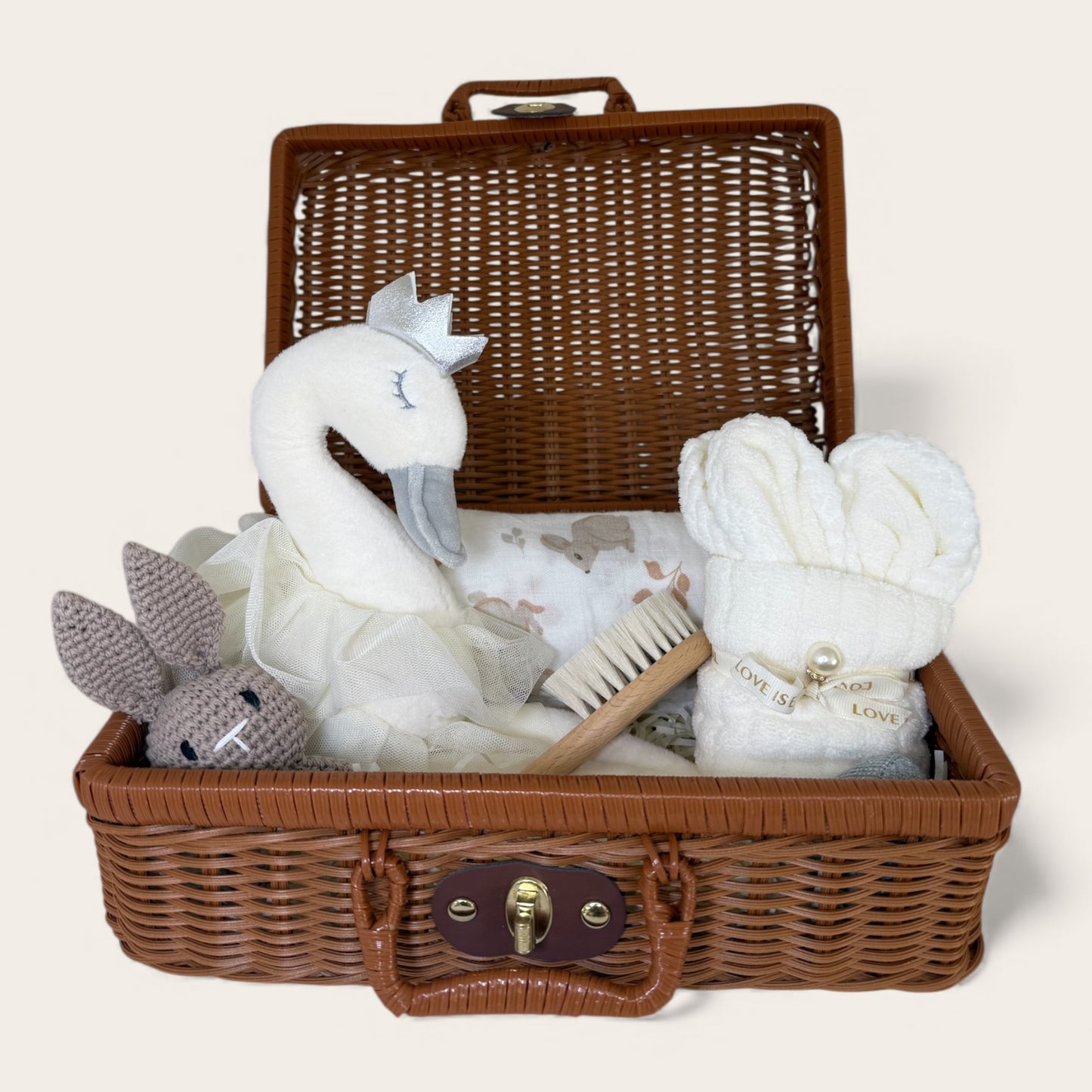 Ivory swan baby gift hamper in a brown wicker keepsake suitcase with plush swan toy, crochet bunny rattle, organic muslin swaddle and baby essentials.