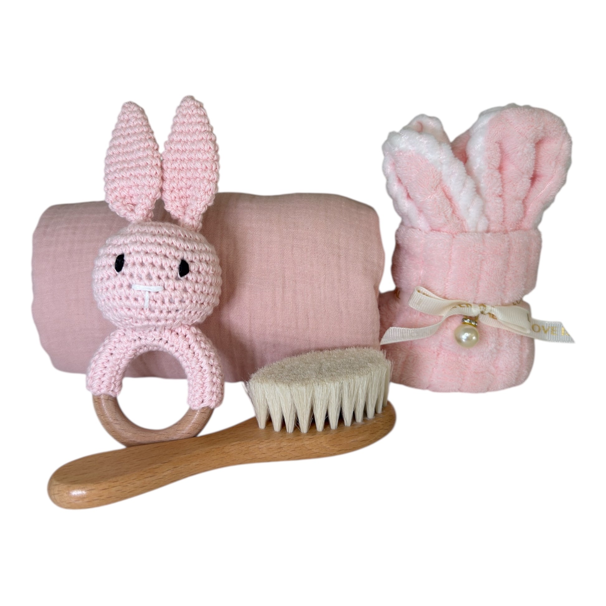 Pink baby gift set including bunny rattle, muslin cloth, rolled baby face cloth and wooden brush on white background