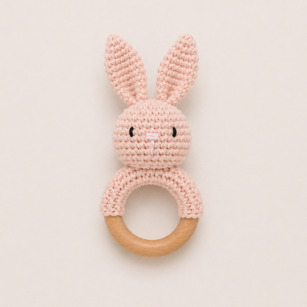 Baby crochet bunny rattle with wooden ring in soft pink on neutral background