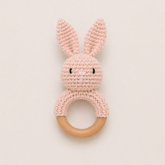 Baby crochet bunny rattle with wooden ring in soft pink on neutral background