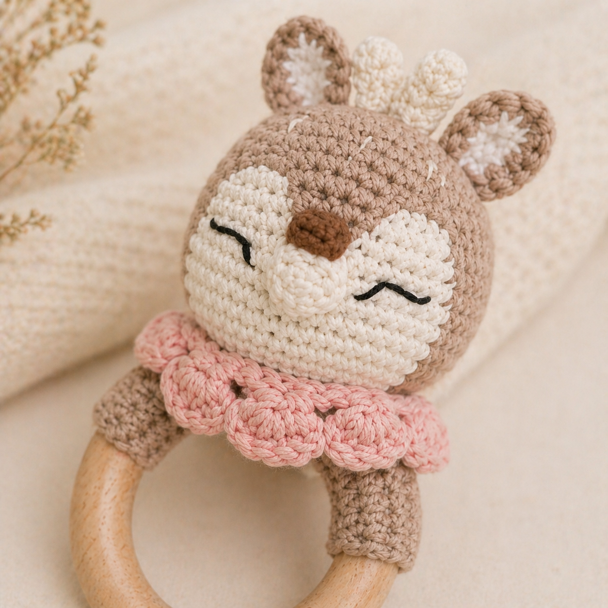 Crochet deer rattle with a pink collar on a soft background