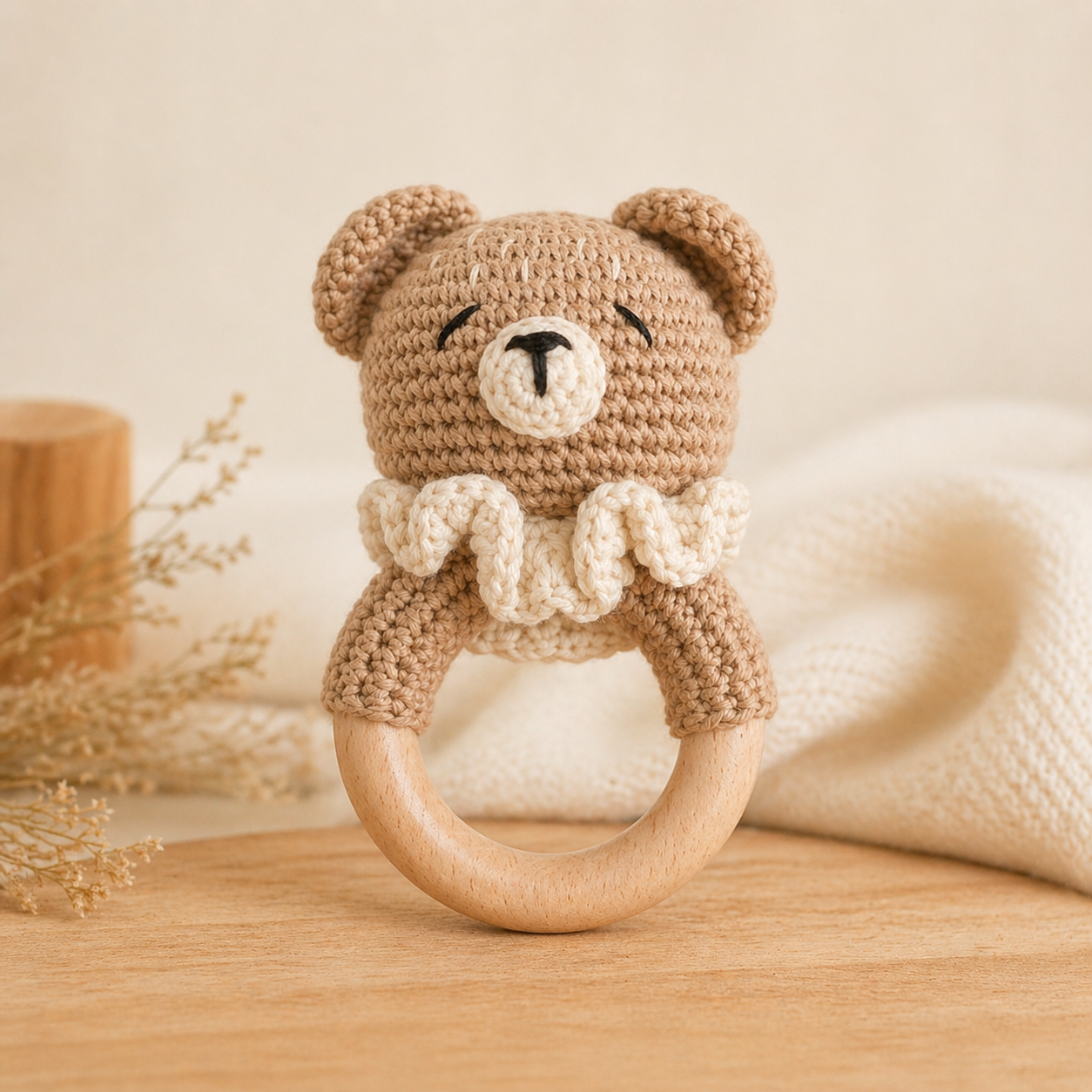 Crocheted teddy bear rattle on a wooden surface with a neutral background