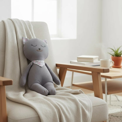 Soft grey kitten baby doll resting on an armchair with a neutral blanket