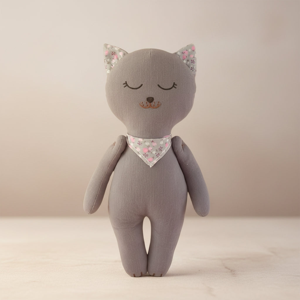 Soft grey kitten baby doll with floral ears and matching neck scarf on a neutral background