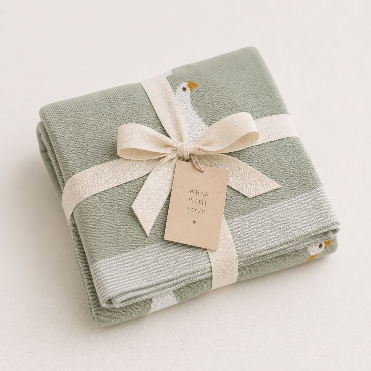 Folded green knitted organic cotton baby blanket with white goose pattern tied with cream ribbon bow, ready to gift by Wrap With Love