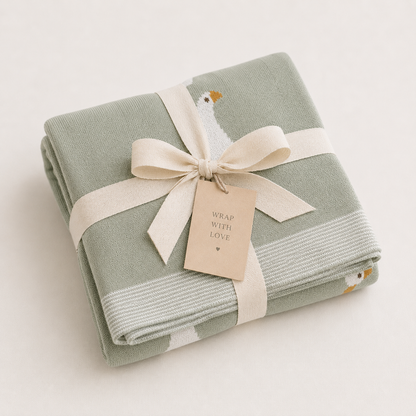 Folded green knitted organic cotton baby blanket with white goose pattern tied with cream ribbon bow, ready to gift by Wrap With Love