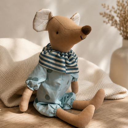 Soft mouse plush toy wearing a sage outfit sitting on a neutral knitted blanket in a boutique nursery setting
