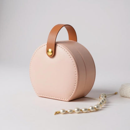 Round pink jewellery box with handle, structured design and minimalist finish.