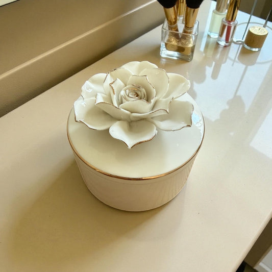 White ceramic flower jewellery box with sculpted floral lid and gold accents displayed on a vanity surface.