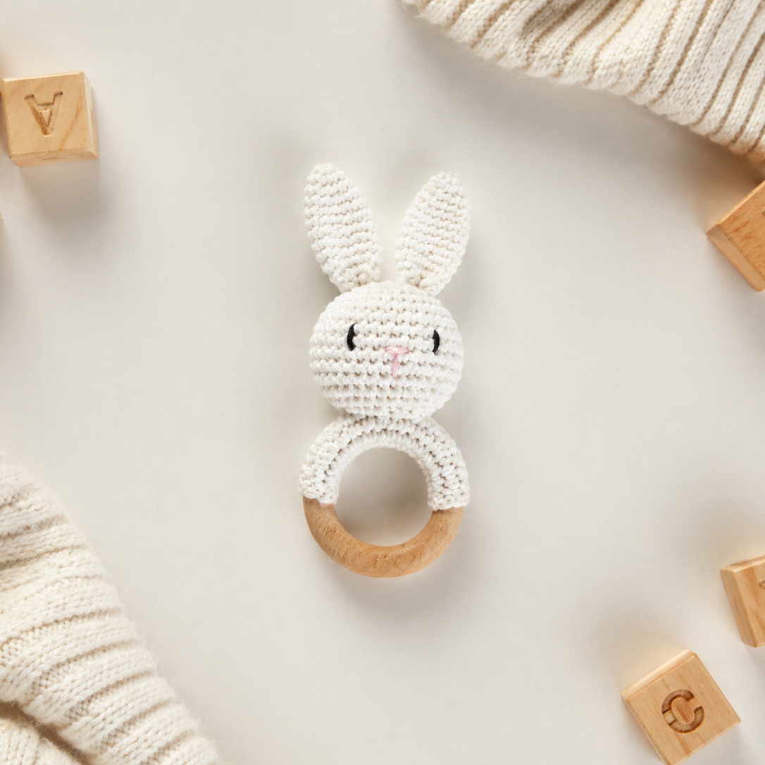 White crocheted bunny rattle with wooden ring on a light background with wooden blocks.