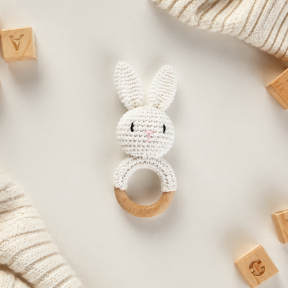 White crocheted bunny rattle with wooden ring on a light background with wooden blocks.